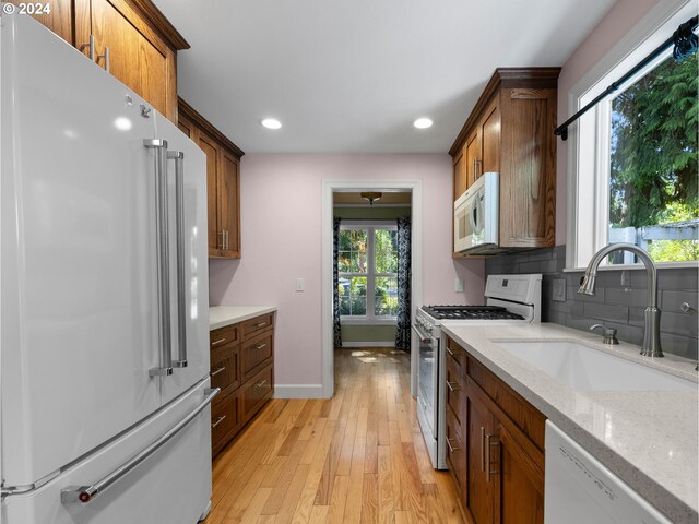 kitchen with decorative backsplash, sink, light stone counters, light wood-type flooring, and white appliances