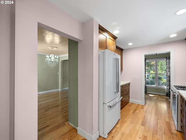 kitchen with light hardwood / wood-style flooring, hanging light fixtures, gas range oven, and white refrigerator