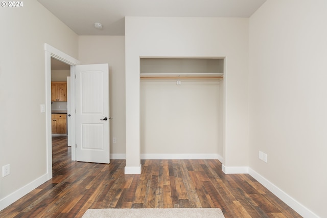 unfurnished bedroom featuring a closet, dark wood-style flooring, and baseboards