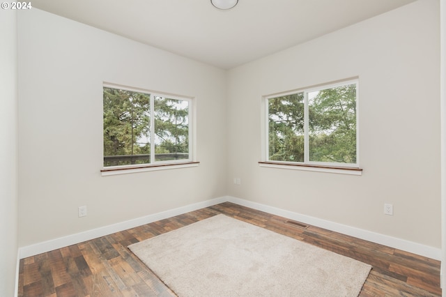 spare room featuring dark wood-type flooring, visible vents, and baseboards