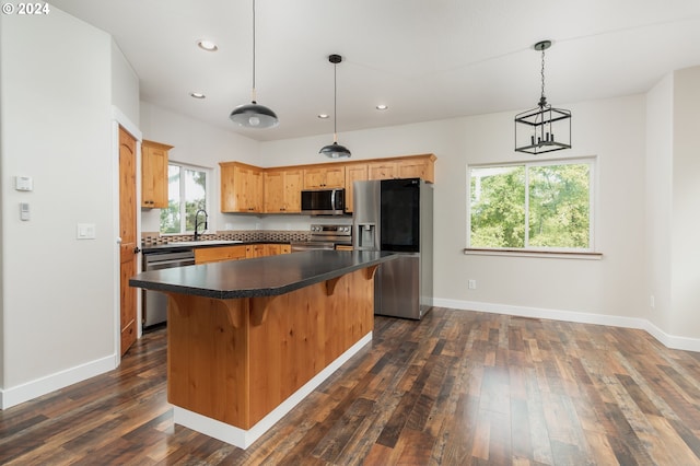 kitchen featuring dark wood finished floors, stainless steel appliances, dark countertops, hanging light fixtures, and a kitchen island