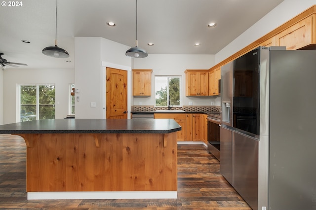 kitchen with a center island, pendant lighting, dark countertops, appliances with stainless steel finishes, and a sink