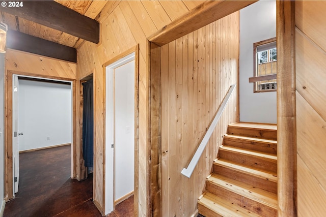stairway featuring wooden walls, wood ceiling, and beamed ceiling