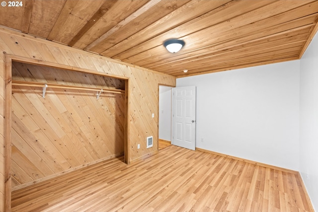 unfurnished bedroom featuring wooden walls, wood finished floors, visible vents, a closet, and wooden ceiling