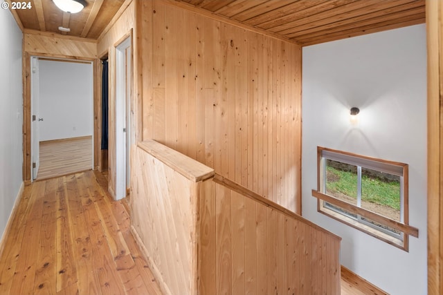 corridor with an upstairs landing, light wood-style floors, wooden ceiling, and wood walls