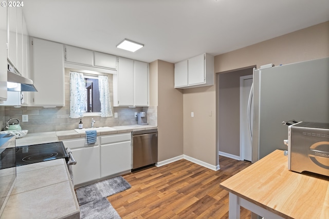 kitchen with appliances with stainless steel finishes, backsplash, tile countertops, and white cabinetry