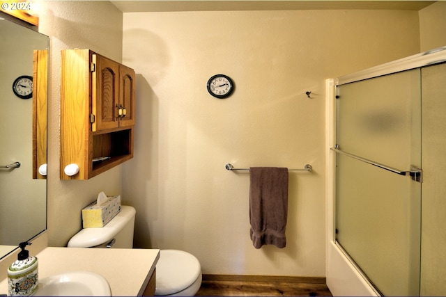 full bathroom with hardwood / wood-style flooring, bath / shower combo with glass door, vanity, and toilet