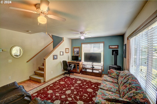 living room with a textured ceiling, ceiling fan, and a wood stove