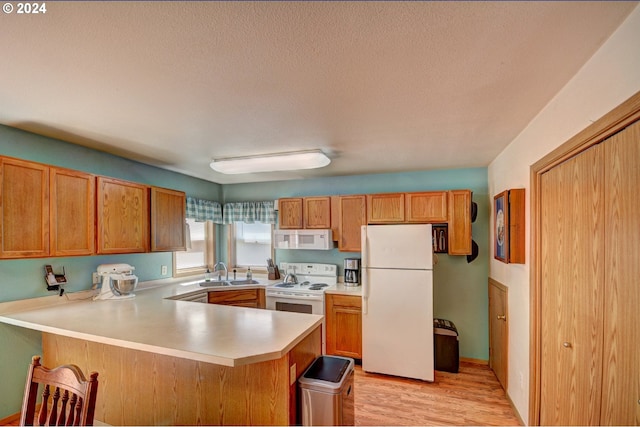 kitchen featuring sink, white appliances, light hardwood / wood-style flooring, a textured ceiling, and kitchen peninsula