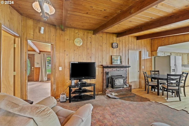 living room with wood ceiling, beam ceiling, a wood stove, and wood walls