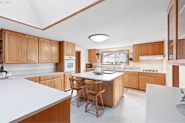 970 Kalmia St, Junction City, OR 97448 - kitchen featuring white oven, under cabinet range hood, light countertops, a breakfast bar, and a textured ceiling