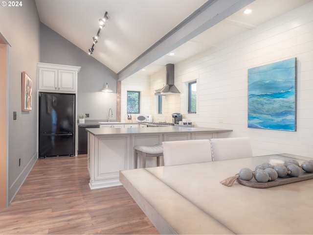 kitchen featuring rail lighting, white cabinets, light hardwood / wood-style floors, wall chimney range hood, and black fridge