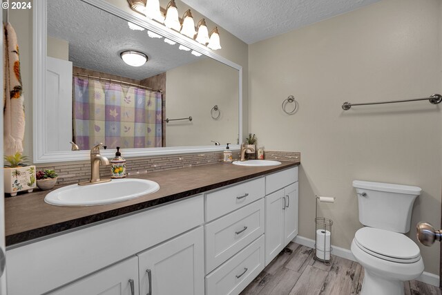 bathroom featuring hardwood / wood-style flooring, toilet, vanity, a textured ceiling, and tasteful backsplash