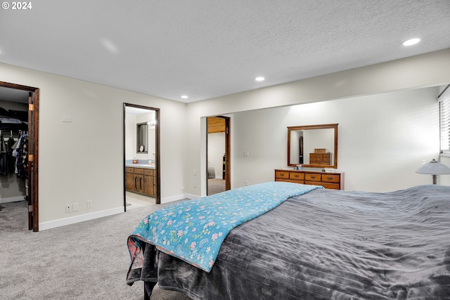 bedroom featuring a walk in closet, light carpet, a textured ceiling, and ensuite bath