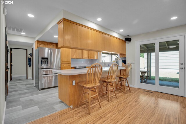 kitchen with light hardwood / wood-style flooring, kitchen peninsula, stainless steel appliances, and a kitchen breakfast bar