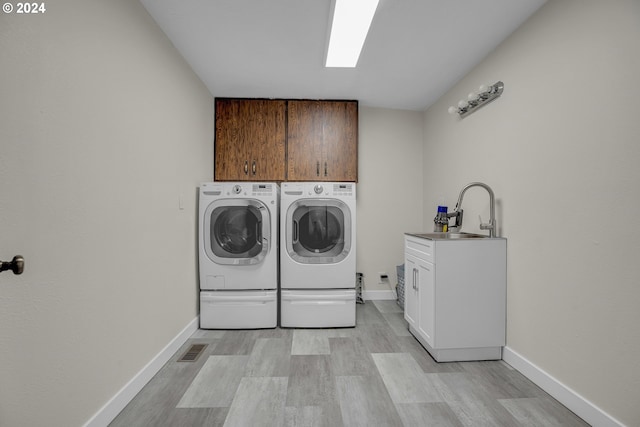 laundry room featuring cabinets, sink, washing machine and clothes dryer, and light hardwood / wood-style floors