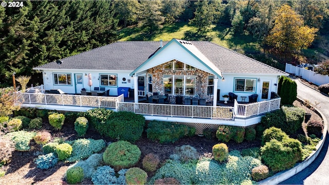 back of house featuring stone siding, a deck, outdoor lounge area, and a shingled roof