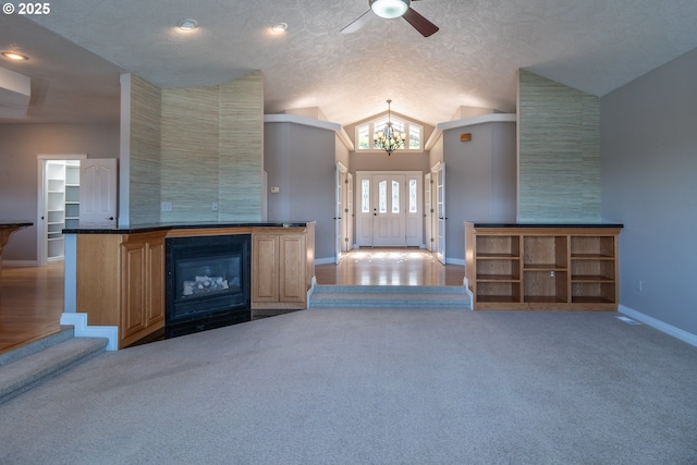 unfurnished living room with baseboards, vaulted ceiling, carpet flooring, a glass covered fireplace, and a textured ceiling