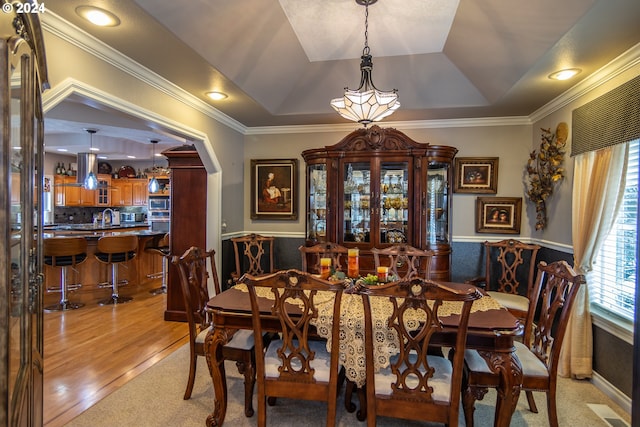 dining room with a tray ceiling, wainscoting, arched walkways, and light wood-type flooring