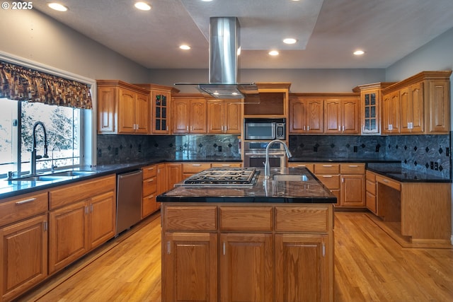 kitchen featuring light wood finished floors, brown cabinets, island exhaust hood, stainless steel appliances, and a sink