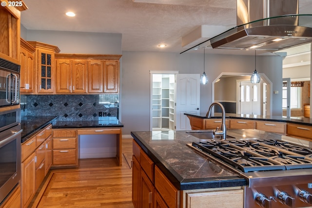 kitchen featuring stainless steel oven, a sink, brown cabinetry, and wall chimney range hood