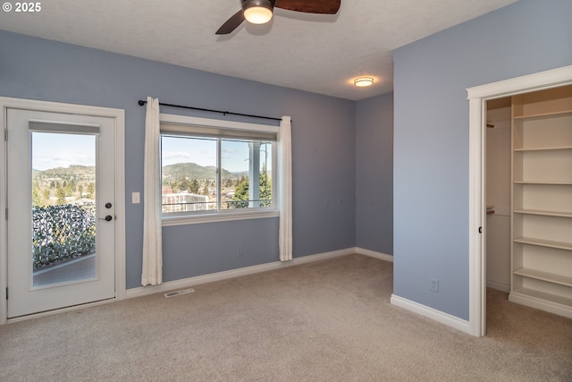 unfurnished bedroom with a spacious closet, baseboards, carpet floors, a textured ceiling, and access to outside