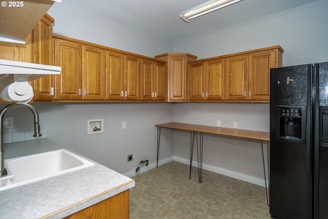 kitchen with a sink, brown cabinets, black fridge, and light countertops