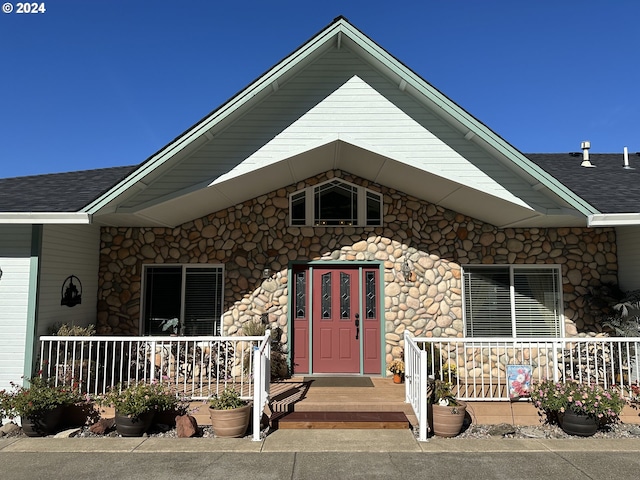 doorway to property featuring a porch and roof with shingles