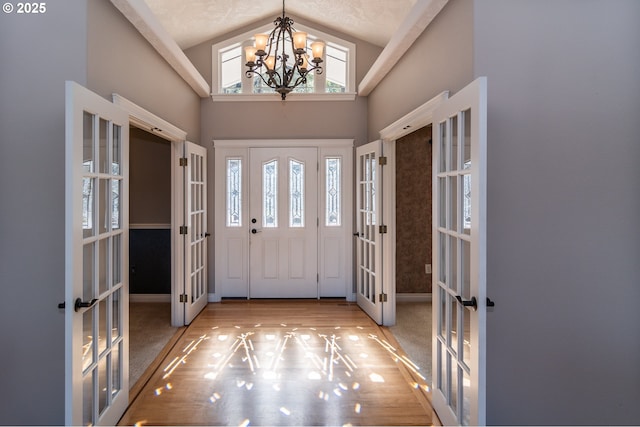 carpeted foyer with french doors, wood finished floors, high vaulted ceiling, and a chandelier