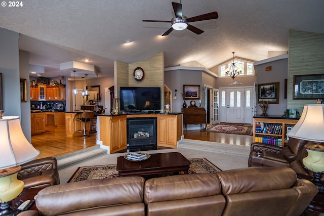 living room with lofted ceiling, light hardwood / wood-style floors, a large fireplace, a textured ceiling, and ceiling fan with notable chandelier