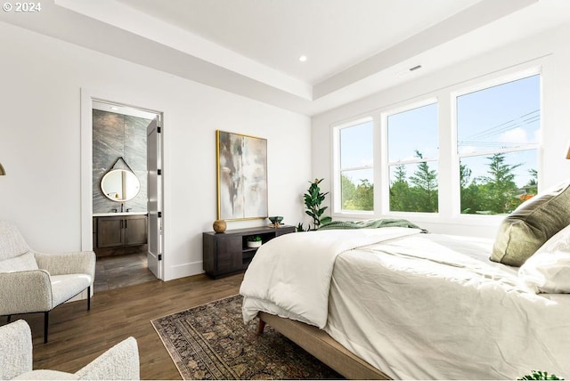 bedroom featuring dark hardwood / wood-style floors, a tray ceiling, and ensuite bathroom