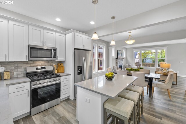 kitchen featuring decorative backsplash, appliances with stainless steel finishes, light wood-type flooring, pendant lighting, and white cabinetry