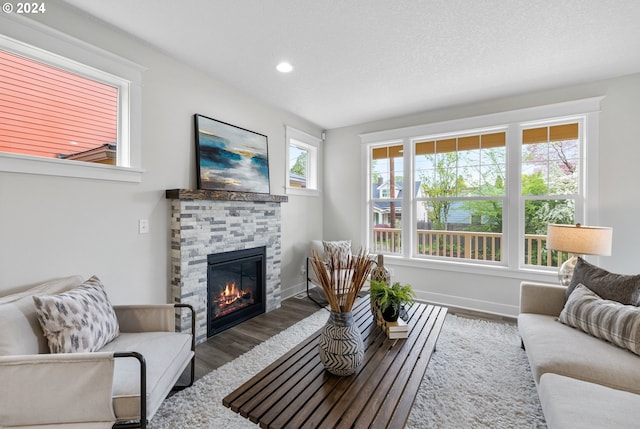 living room featuring wood-type flooring, a textured ceiling, a stone fireplace, and a healthy amount of sunlight