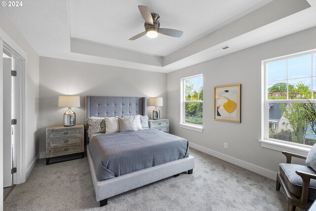 bedroom with a tray ceiling, ceiling fan, and light carpet