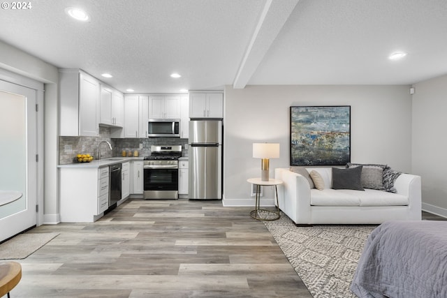 kitchen featuring white cabinetry, sink, backsplash, appliances with stainless steel finishes, and light wood-type flooring