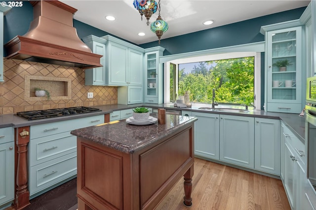 kitchen with a sink, a center island, stainless steel gas stovetop, custom range hood, and backsplash