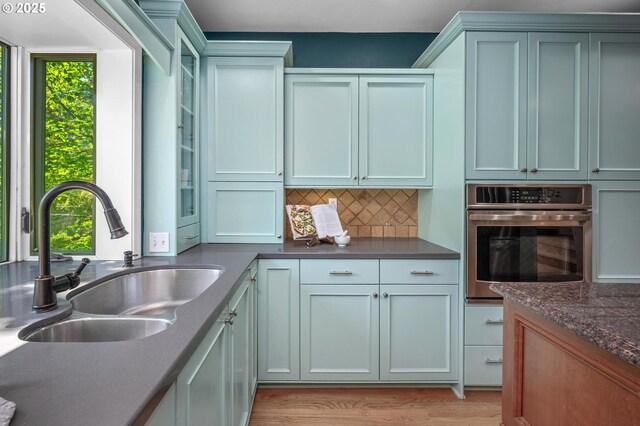 kitchen featuring glass insert cabinets, oven, a sink, light wood finished floors, and backsplash