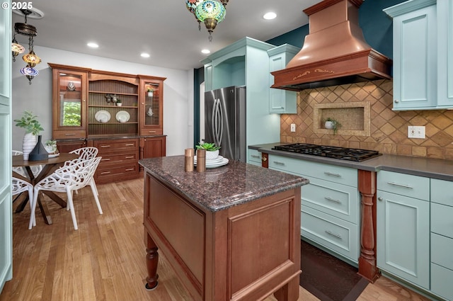 kitchen with freestanding refrigerator, premium range hood, gas cooktop, a center island, and backsplash