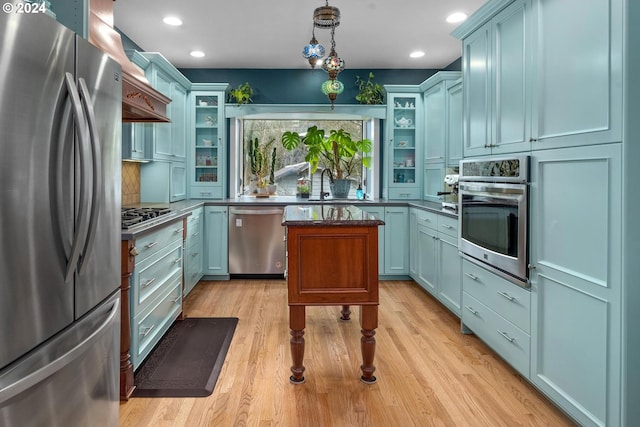 kitchen with blue cabinets, sink, hanging light fixtures, appliances with stainless steel finishes, and light hardwood / wood-style floors