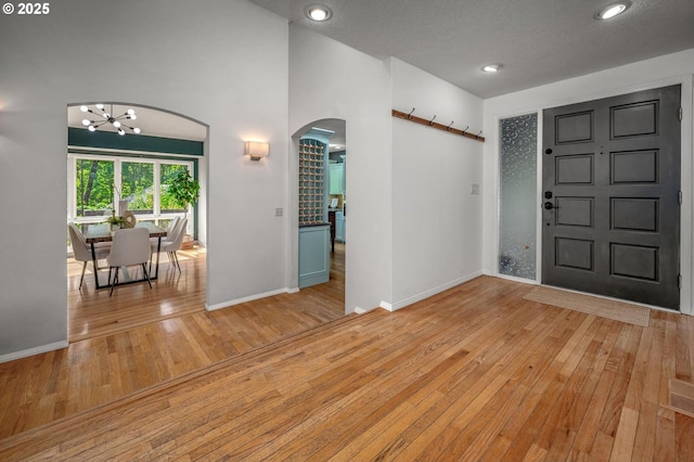foyer entrance featuring an inviting chandelier, arched walkways, hardwood / wood-style floors, recessed lighting, and baseboards