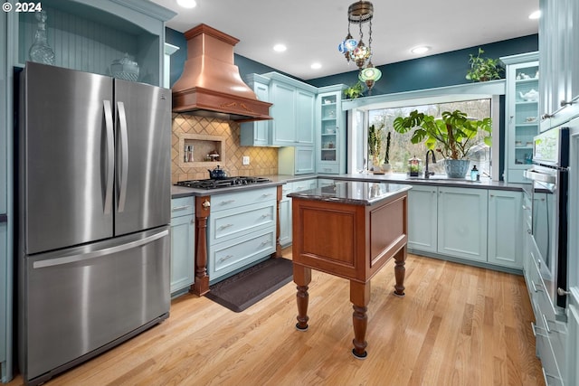 kitchen with stainless steel appliances, backsplash, decorative light fixtures, custom exhaust hood, and light wood-type flooring