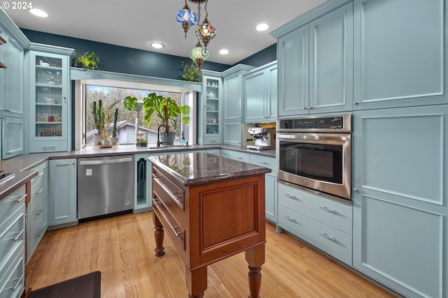 kitchen with dark stone counters, sink, hanging light fixtures, light wood-type flooring, and appliances with stainless steel finishes