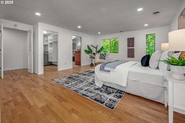 bedroom with light wood-style floors, a walk in closet, and a textured ceiling