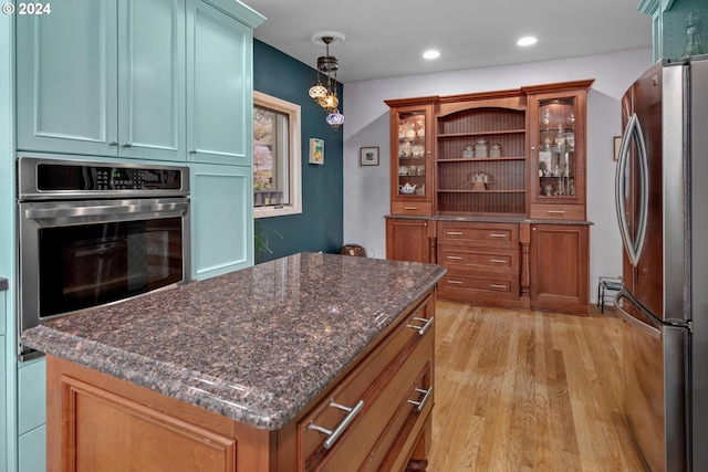 kitchen with a center island, hanging light fixtures, dark stone countertops, light wood-type flooring, and stainless steel refrigerator