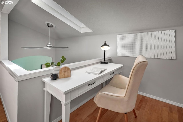 office space featuring a skylight, baseboards, a ceiling fan, and wood finished floors