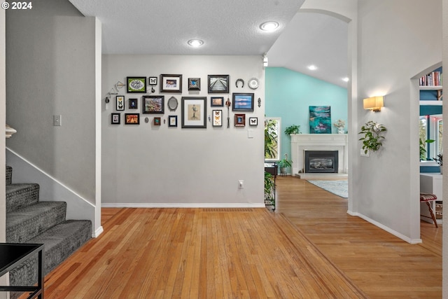 corridor featuring lofted ceiling, light hardwood / wood-style floors, and a textured ceiling