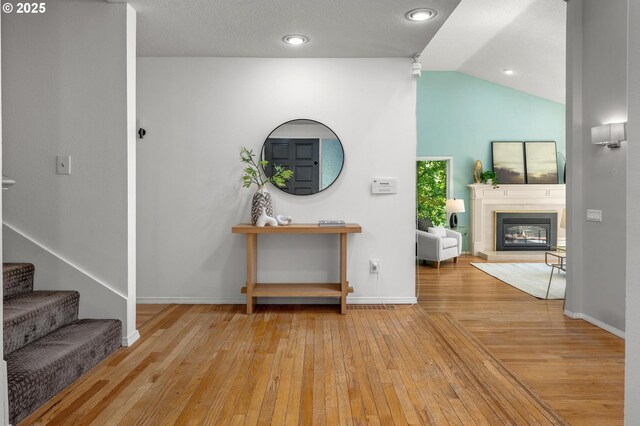 interior space with baseboards, vaulted ceiling, a glass covered fireplace, and hardwood / wood-style floors