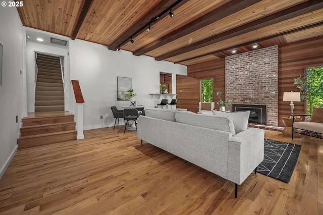 living room featuring track lighting, baseboards, wooden walls, stairway, and light wood-style flooring