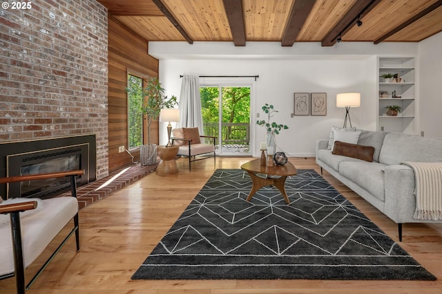 living room featuring wood walls, a brick fireplace, beam ceiling, wood ceiling, and light wood finished floors