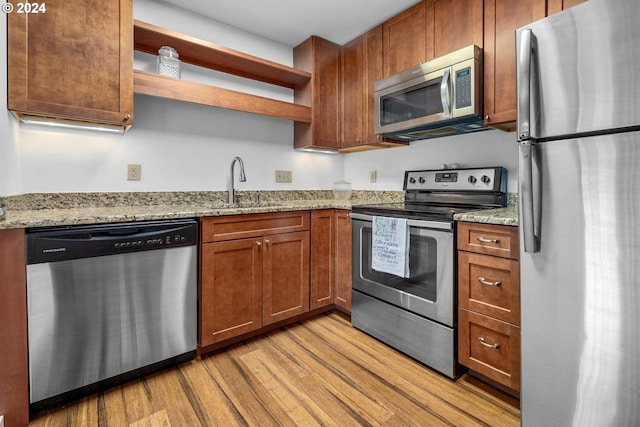 kitchen featuring light stone counters, sink, stainless steel appliances, and light hardwood / wood-style flooring